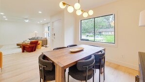 Un espace repas moderne avec une table et des chaises en bois, une grande fenêtre donnant sur l’extérieur et un luminaire au plafond.