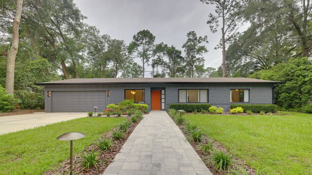 Une maison moderne à deux étages avec une allée pavée menant à un garage.
