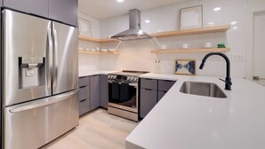 Une cuisine moderne dotée d’appareils électroménagers en acier inoxydable, d’étagères en bois et d’un grand évier.