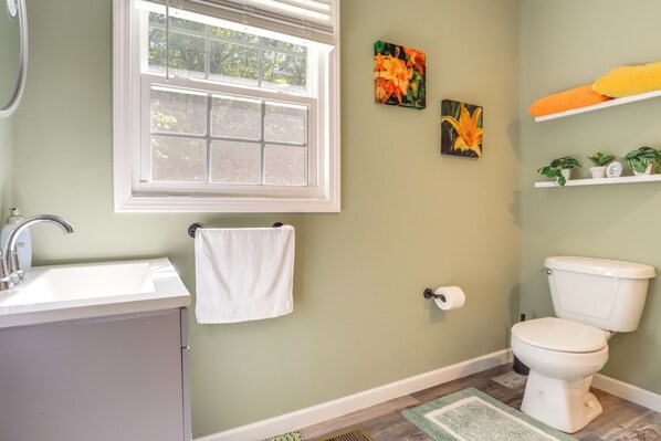 Une salle de bain avec un lavabo blanc, des toilettes, une fenêtre et une serviette accrochée au mur.