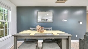 Un coin repas avec une table dressée pour quatre personnes, un mur sombre, un miroir et une fenêtre donnant sur des arbres.
