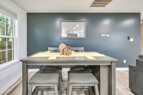 A dining area with a table set for four, a dark wall, a mirror, and a window with a view of trees. - Home w/ Hot Tub, Playset & Grills in Clarksville! (Clarksville)