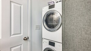 Une buanderie équipée de deux machines à laver à chargement frontal superposées et d’une barrière en tissu gris.