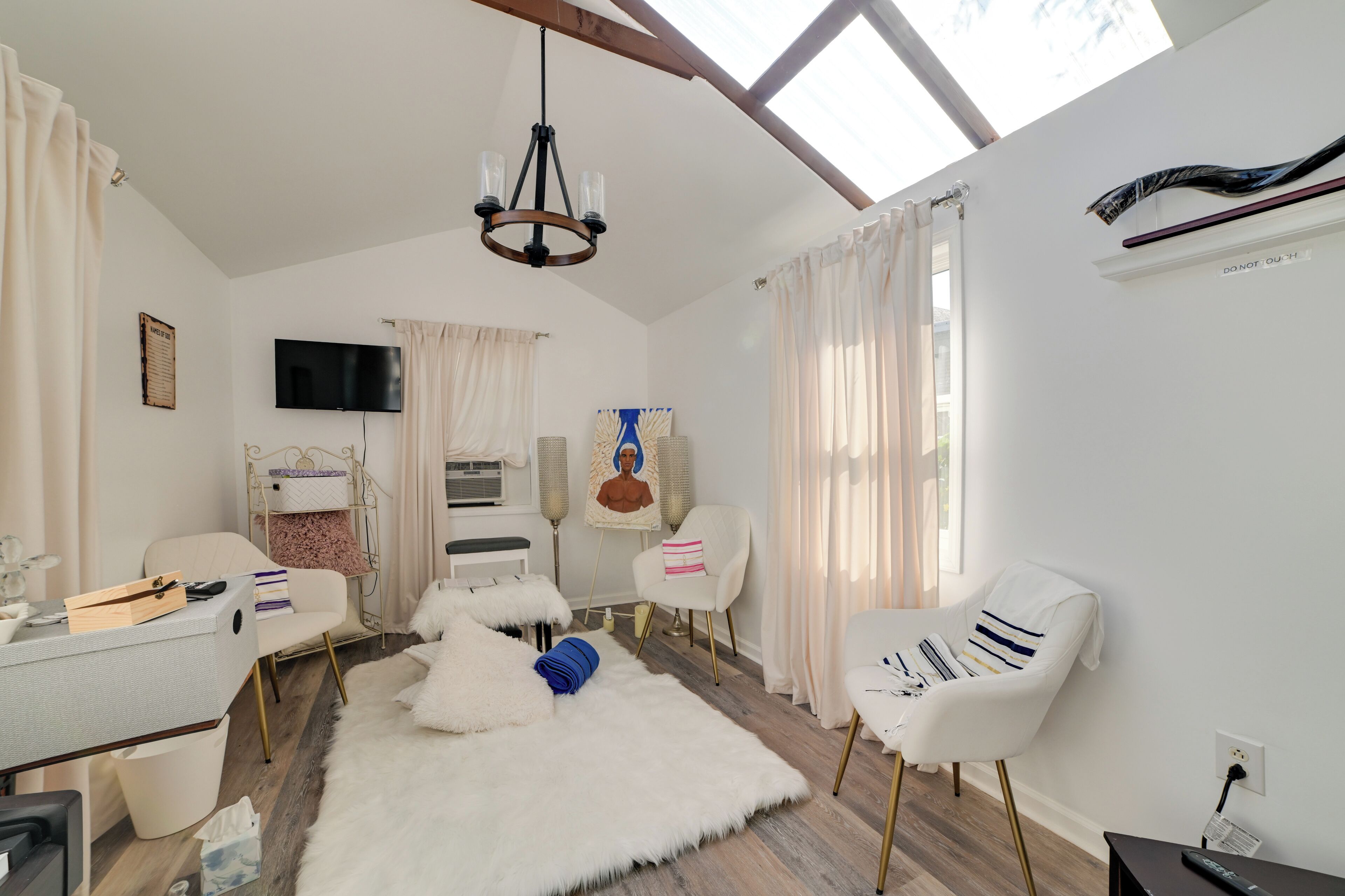 A modern living room with a flat-screen TV, a chandelier, and a large window with curtains.