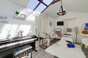 A room with a piano, a white fur rug, a chair, a television, and a painting. - Home w/ Hot Tub, Playset & Grills in Clarksville! (Clarksville)