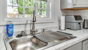 Une cuisine équipée d’un évier en acier inoxydable, d’une fenêtre donnant sur les arbres et d’une machine à café posée sur le plan de travail.