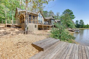 A large wooden cabin with multiple decks and a dock extending into a lake, surrounded by trees. - Modern Home Near Lake Martin: Fishing Pond On-site (Eclectic)