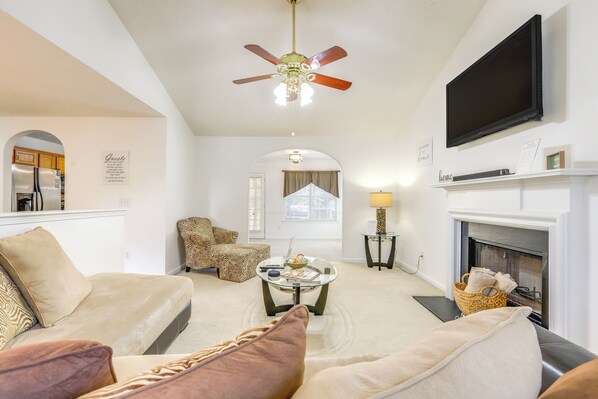 A living room with a sofa, armchair, coffee table, fireplace, television, and ceiling fan.