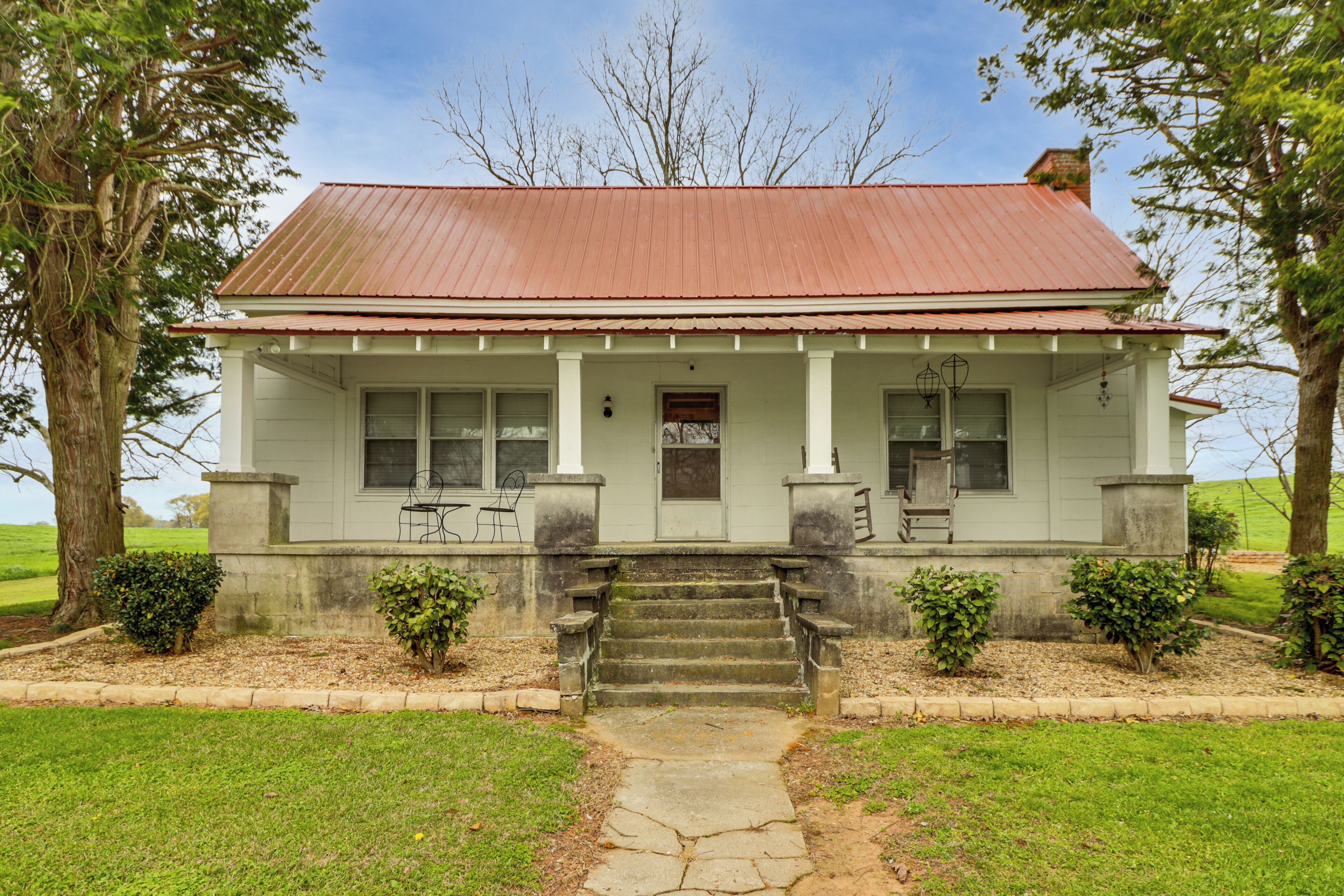 A two-story house with a red roof, a front porch with steps, and a small garden with bushes.