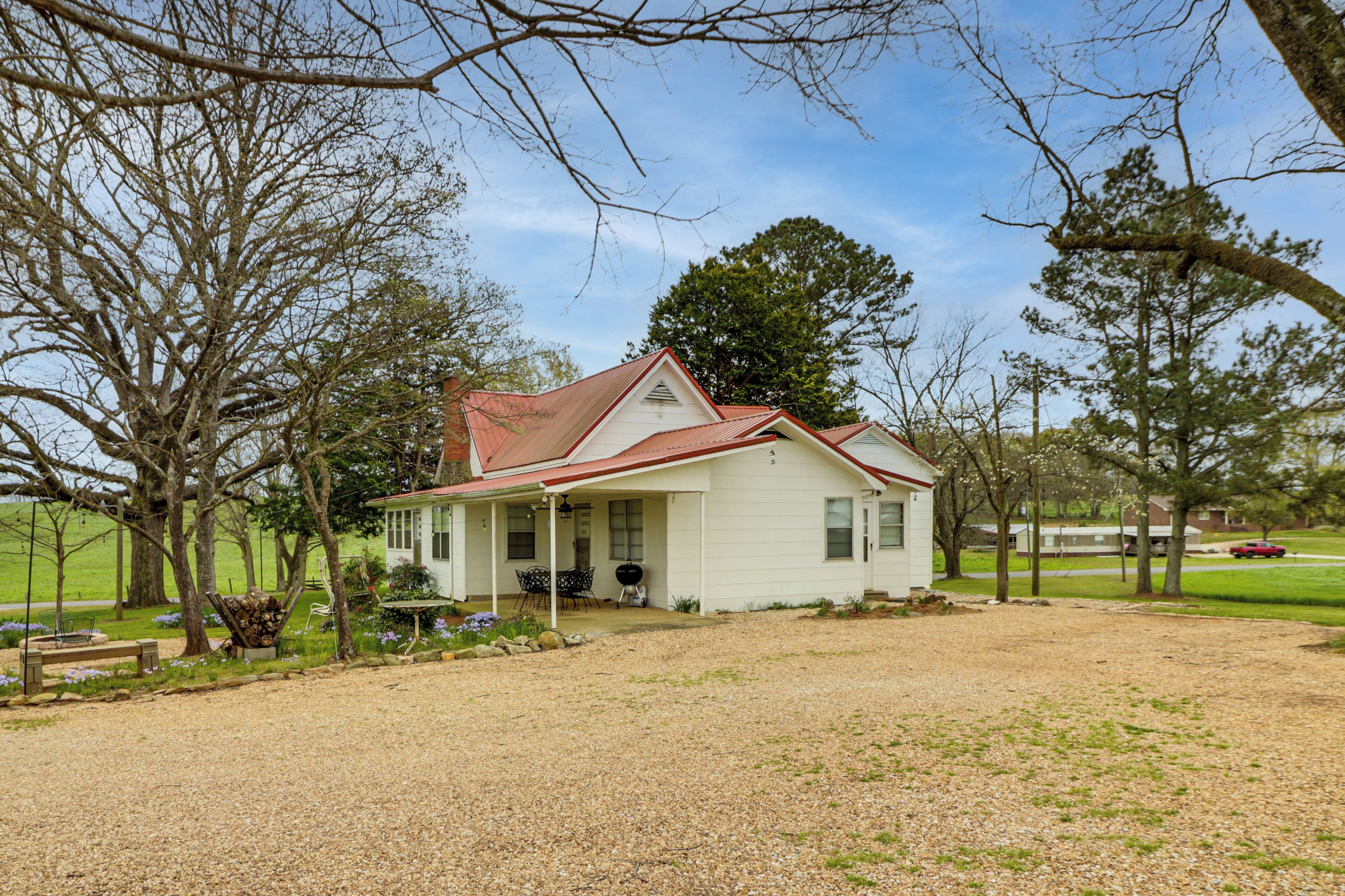 A white house with a red roof, surrounded by trees and a gravel driveway.