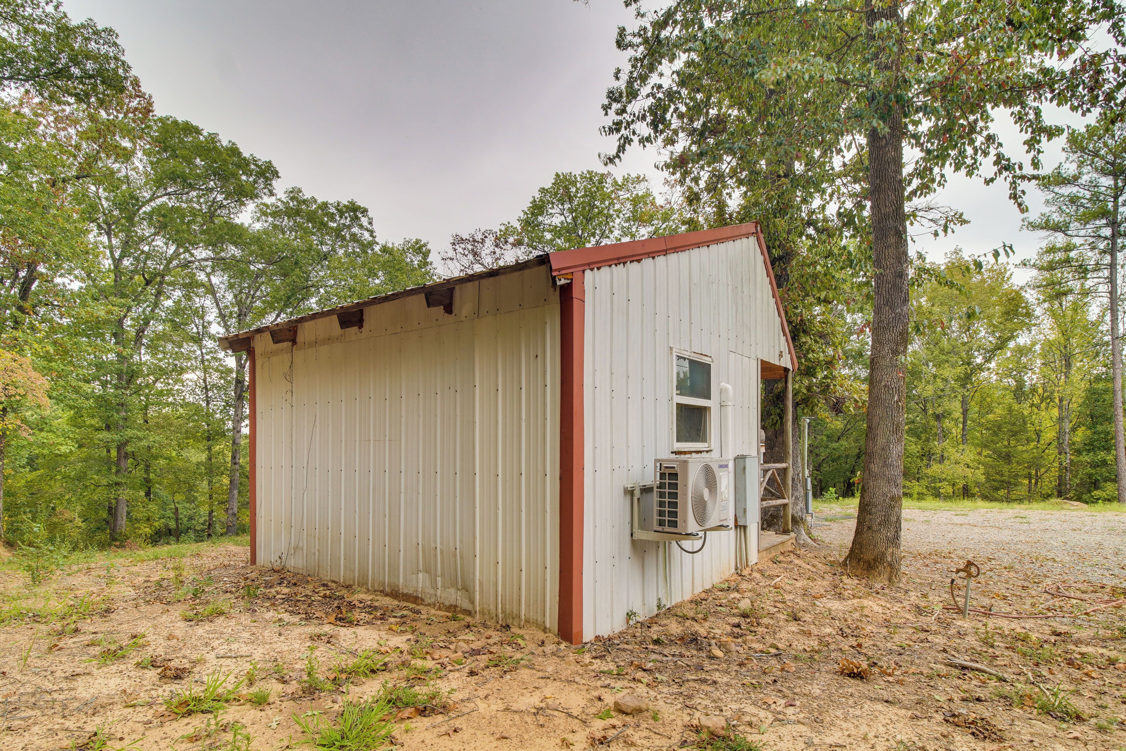 A small, single-story metal shed with a red roof, a window, and an air conditioning unit mounted on the side.