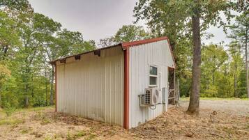 A small, single-story metal shed with a red roof, a window, and an air conditioning unit mounted on the side.