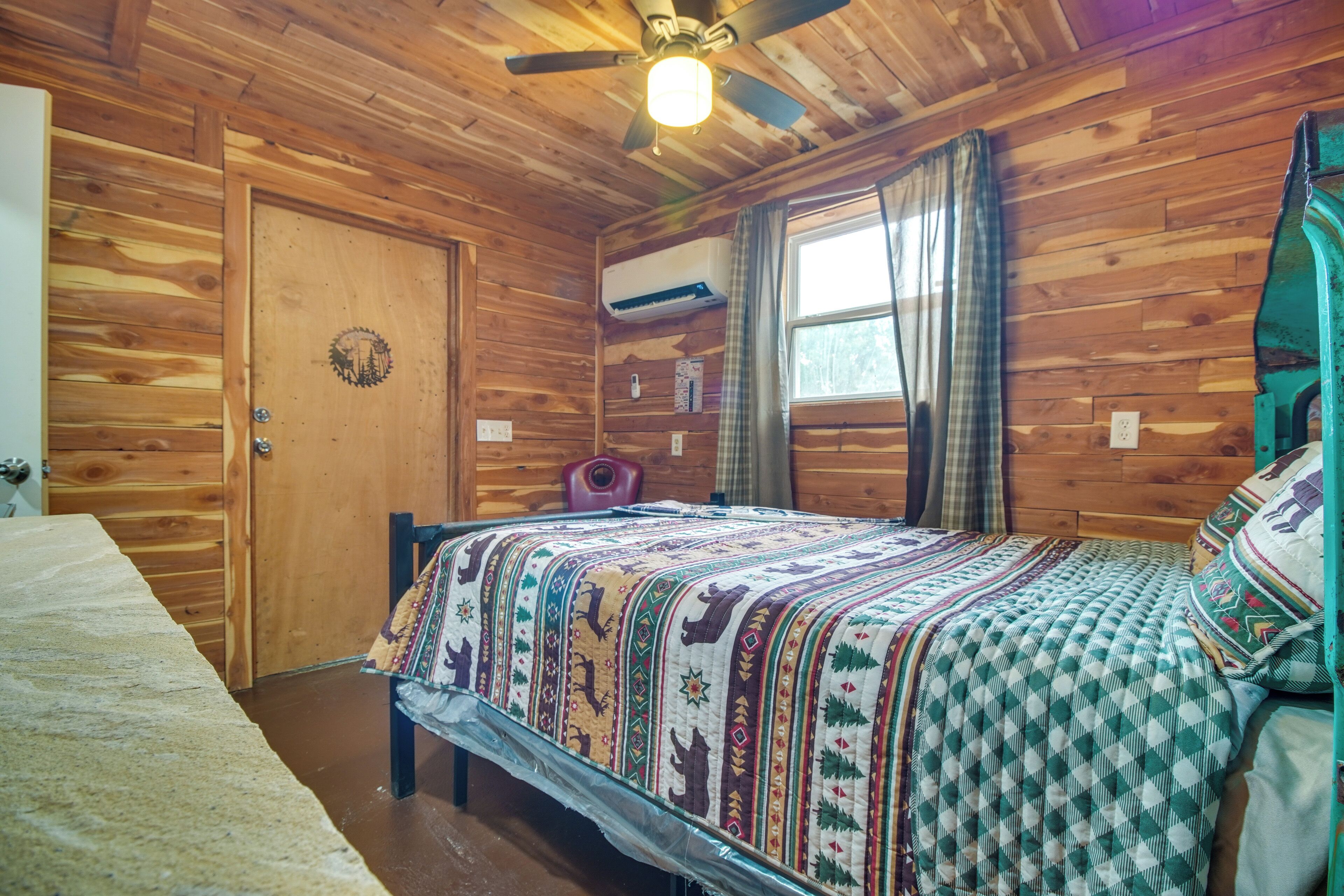 A wooden cabin bedroom with a bed, a ceiling fan, and a window with curtains.