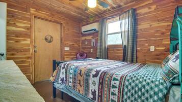 A wooden cabin bedroom with a bed, a ceiling fan, and a window with curtains.
