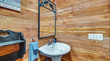A wooden-paneled bathroom with a white sink, a mirror, and a wooden bench.