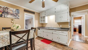 A kitchen with white cabinets, a wooden ceiling fan, and a dining area with a table and chairs. - Fire Pit & Grill: Victoria Home Near Downtown (Victoria)