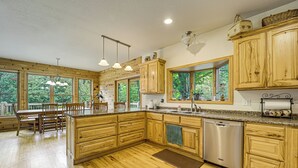 A spacious kitchen with wooden cabinets, a granite countertop, and a dishwasher. - Stunning Riverfront Retreat in Northern Michigan! (Lake City)