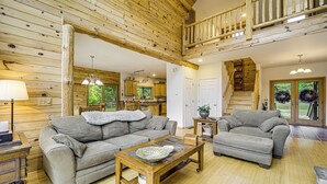 A spacious living area with a wooden ceiling, a sofa set, a coffee table, and a staircase leading to an upper level. - Stunning Riverfront Retreat in Northern Michigan! (Lake City)