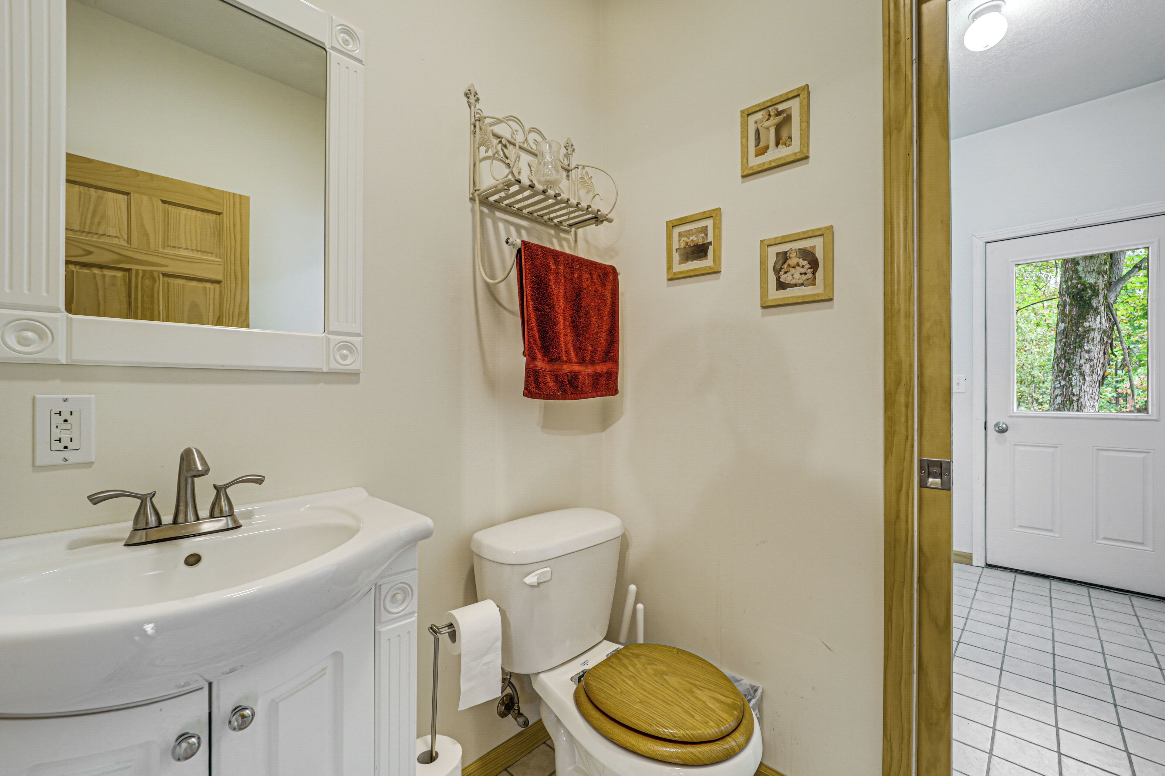 Une salle de bain avec un lavabo blanc, des toilettes avec un abattant en bois, une serviette rouge suspendue à un porte-serviettes et un miroir au-dessus du lavabo.