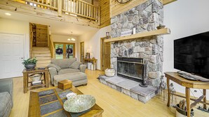 A spacious living room with a stone fireplace, wooden ceiling, and a balcony. - Stunning Riverfront Retreat in Northern Michigan! (Lake City)