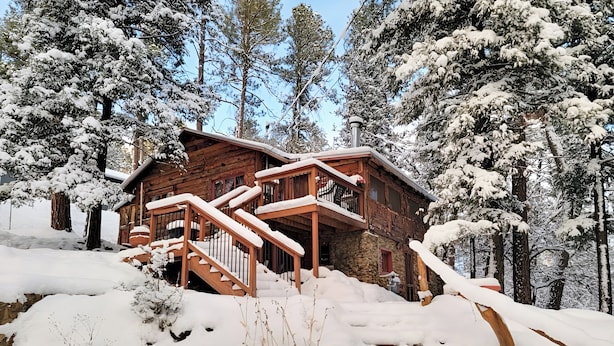 A log cabin with a wooden staircase leading to a porch, surrounded by snow-covered trees. - Cozy Cabin Near Grindstone Lake & Downtown! (Ruidoso)