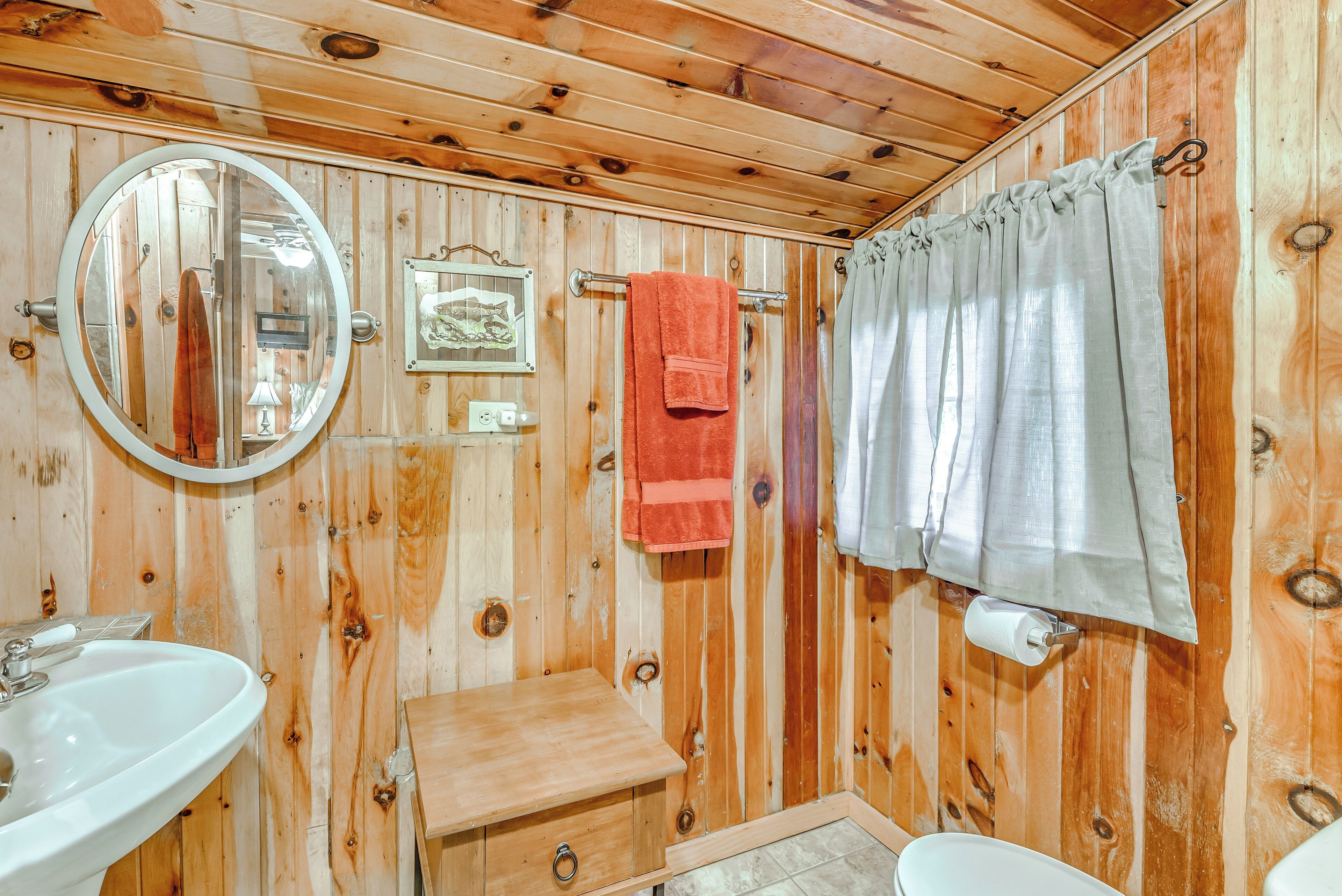 A wooden cabin bathroom with a round mirror, a sink, a small wooden bench, and a shower curtain.