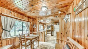 A wooden cabin interior with a dining area, a bench, and a kitchen in the background. - Cozy Cabin Near Grindstone Lake & Downtown! (Ruidoso)