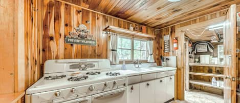 A kitchen with a white stove, wooden walls, and a window.