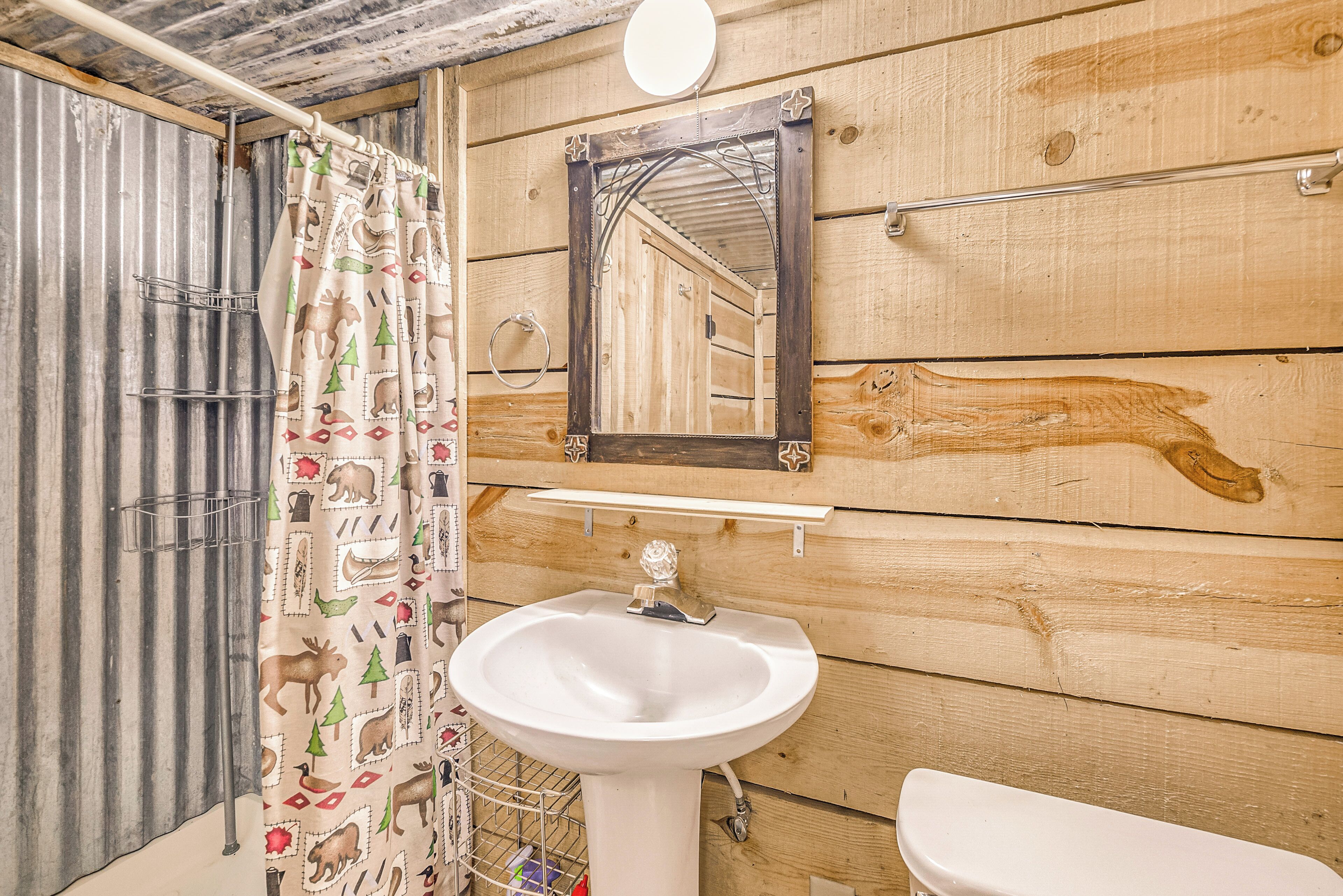 A bathroom with a wooden wall, a white sink, a mirror, and a shower curtain with a moose pattern.
