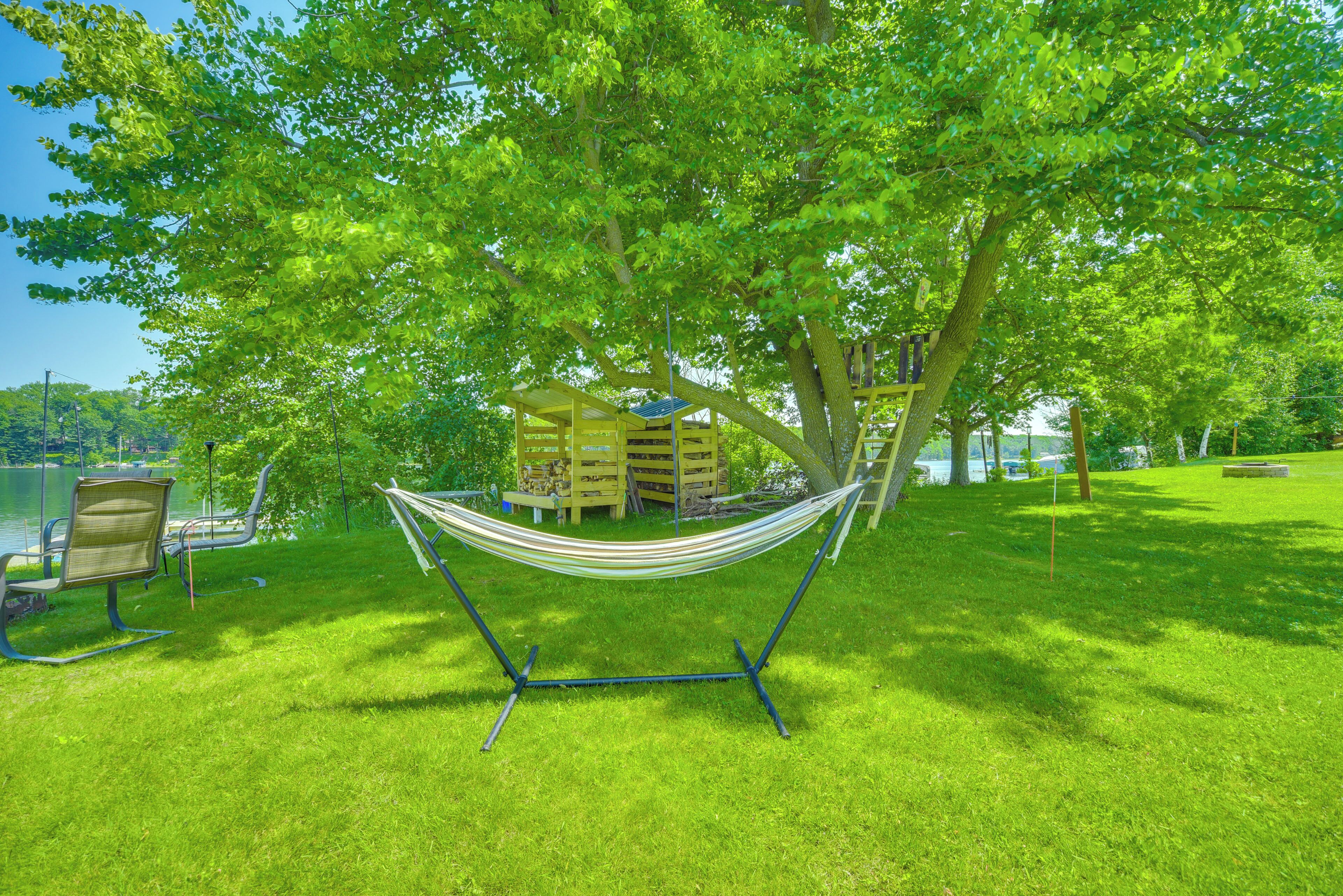 A hammock under a tree, a wooden deck, and a lake in the background.