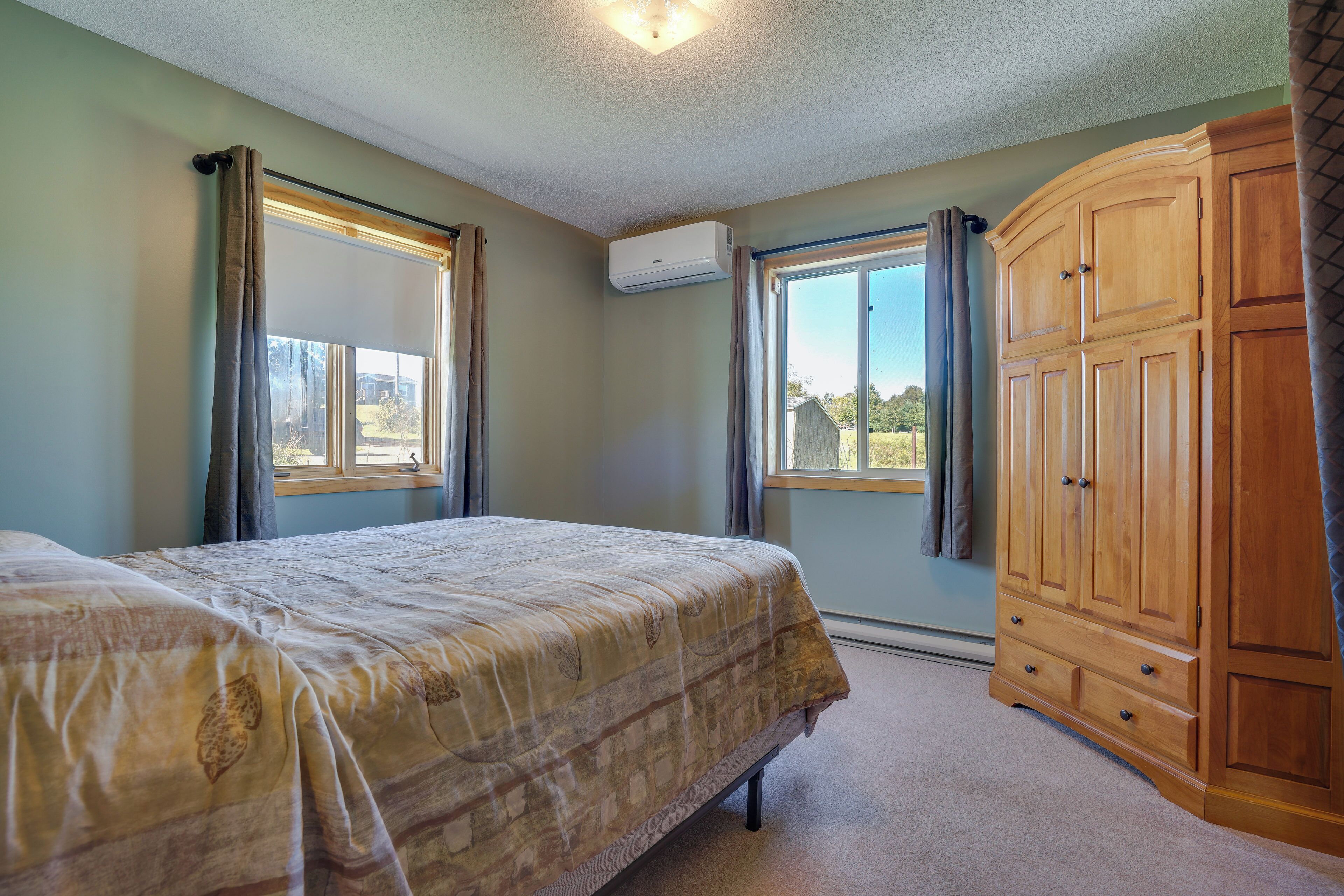 A bedroom with a bed, a wooden wardrobe, and two windows with curtains.