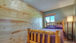 A bedroom with a wooden headboard, a bed with purple bedding, a nightstand, and a window with a view of the outdoors. - 'wet Feet Retreat' Year-round Cabin in Frederic (Frederic)
