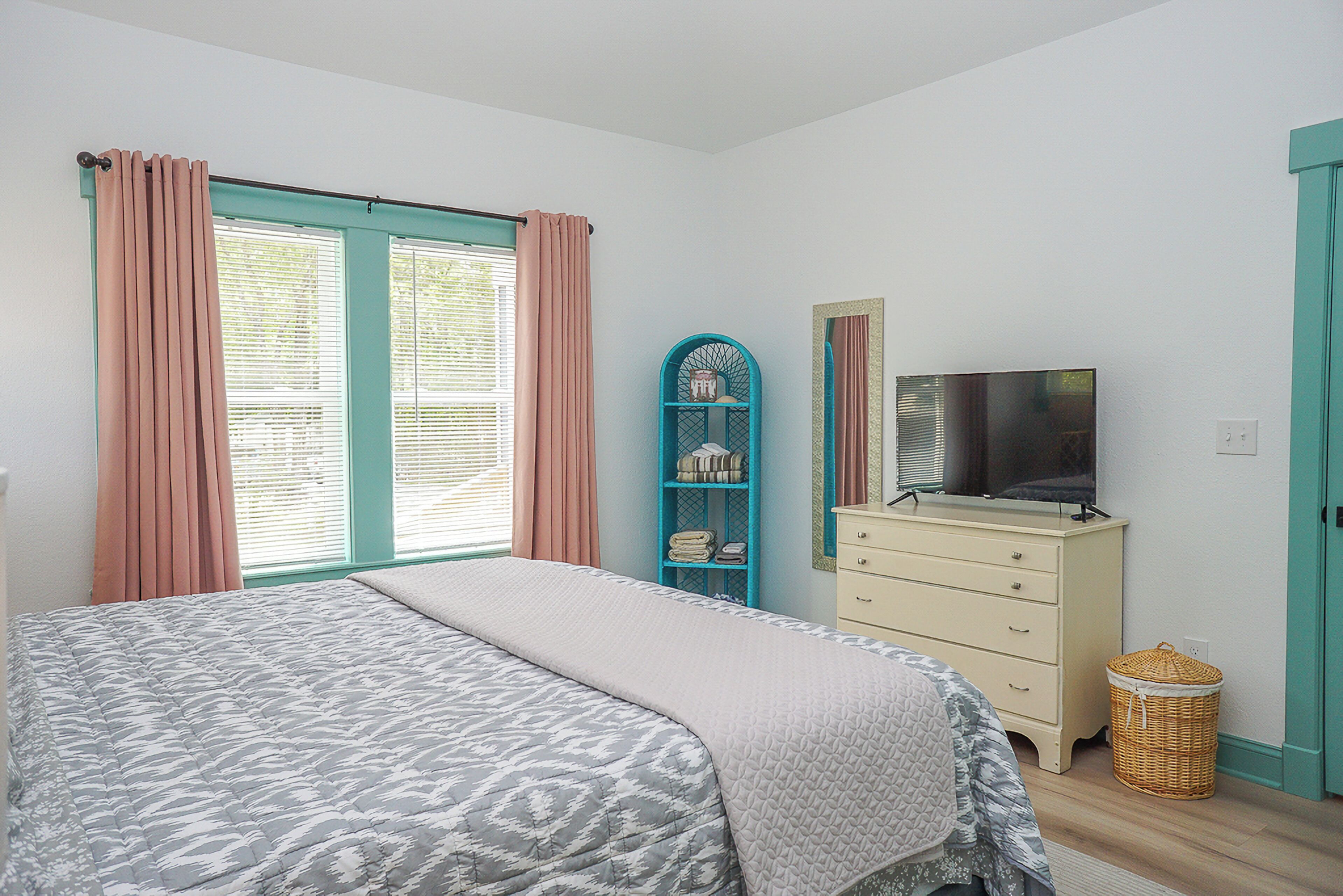 A bedroom with a bed, a dresser, a television, and a window with curtains.