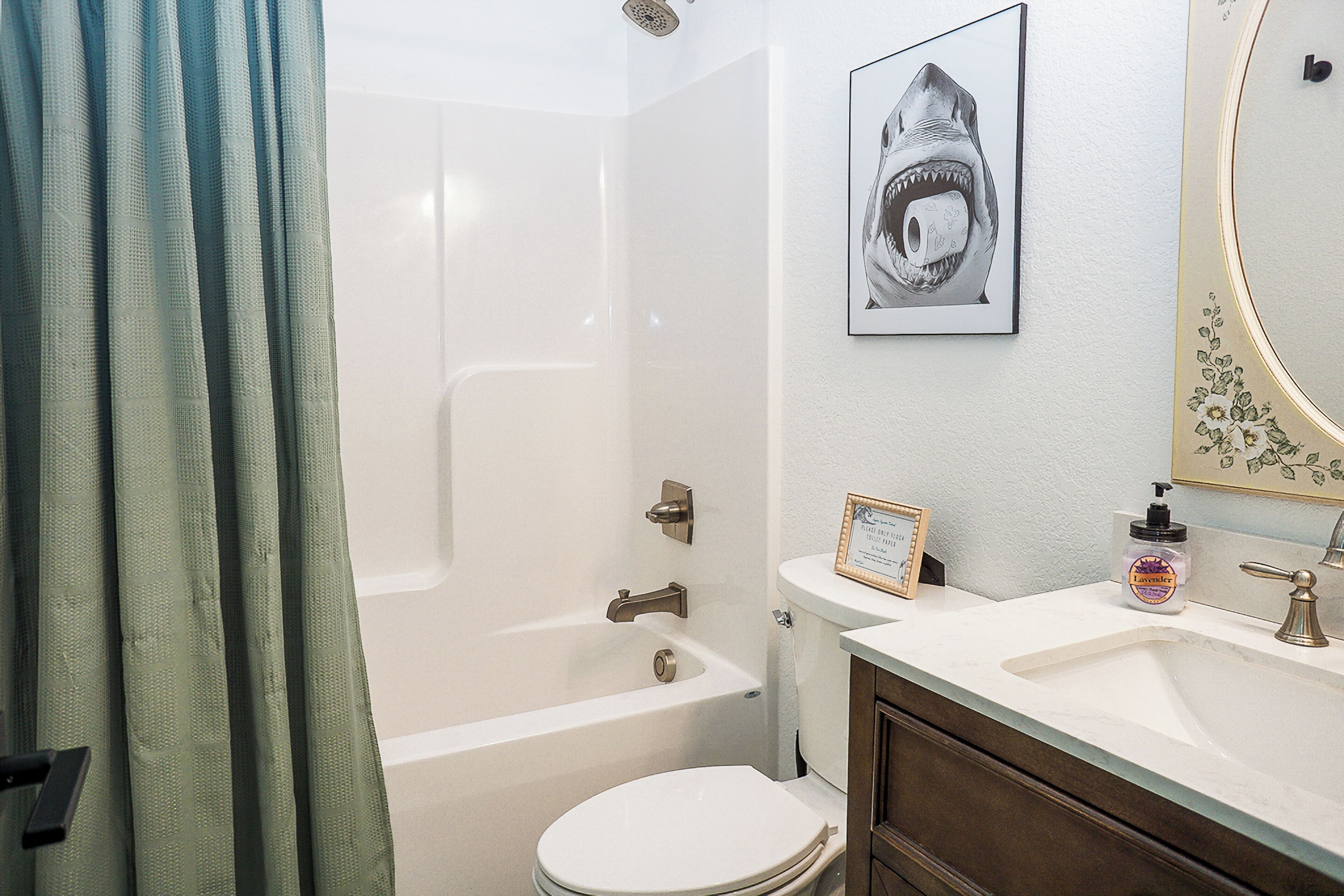 A bathroom with a bathtub, toilet, sink, and a framed shark artwork on the wall.