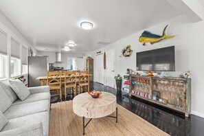 Una sala moderna con un sofá gris, una mesa de centro de madera redonda y un comedor con sillas de madera.