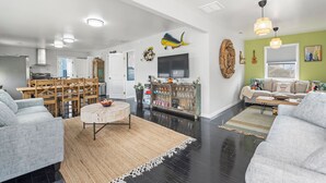A spacious living room with a dining area, a sofa set, a coffee table, and a TV mounted on the wall. - Big Kahuna: Semi-Oceanfront | Tiki Bar | Fire Pit (Avon)