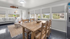 A modern living room with a dining table, sofa, and large windows. - Big Kahuna: Semi-Oceanfront | Tiki Bar | Fire Pit (Avon)
