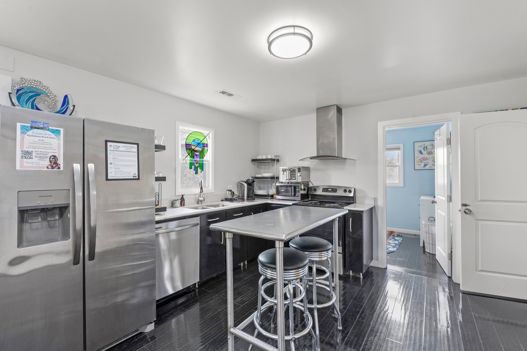 A modern kitchen with stainless steel appliances, a central island with stools, and a door leading to another room.