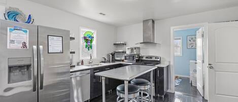 A modern kitchen with stainless steel appliances, a central island with stools, and a door leading to another room.