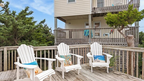 A wooden deck with three white Adirondack chairs, each with a different cushion design. - Big Kahuna: Semi-Oceanfront | Tiki Bar | Fire Pit (Avon)
