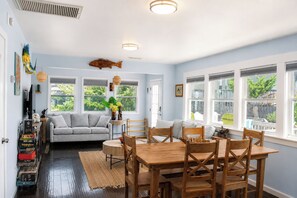 A dining area with a wooden table and chairs, a sofa, and a fish decoration on the wall. - Big Kahuna: Semi-Oceanfront | Tiki Bar | Fire Pit (Avon)