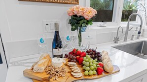 A kitchen counter with a cheese board, wine bottle, and flowers.