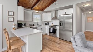 A modern kitchen with white cabinets, stainless steel appliances, and a wooden ceiling.