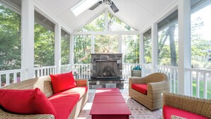 A covered porch with wicker furniture, a stone fireplace, and a ceiling fan.