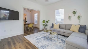 A living room with a sofa, two small side tables, a large rug, and a ceiling fan.