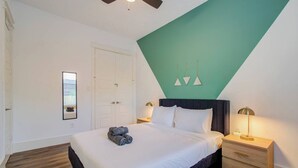 A bedroom with a bed, a nightstand, a wall-mounted lamp, a ceiling fan, and a door.