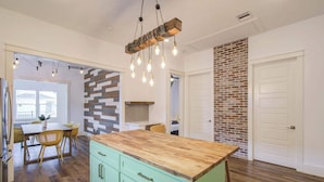 A kitchen with a wooden island, green cabinets, and a brick accent wall.
