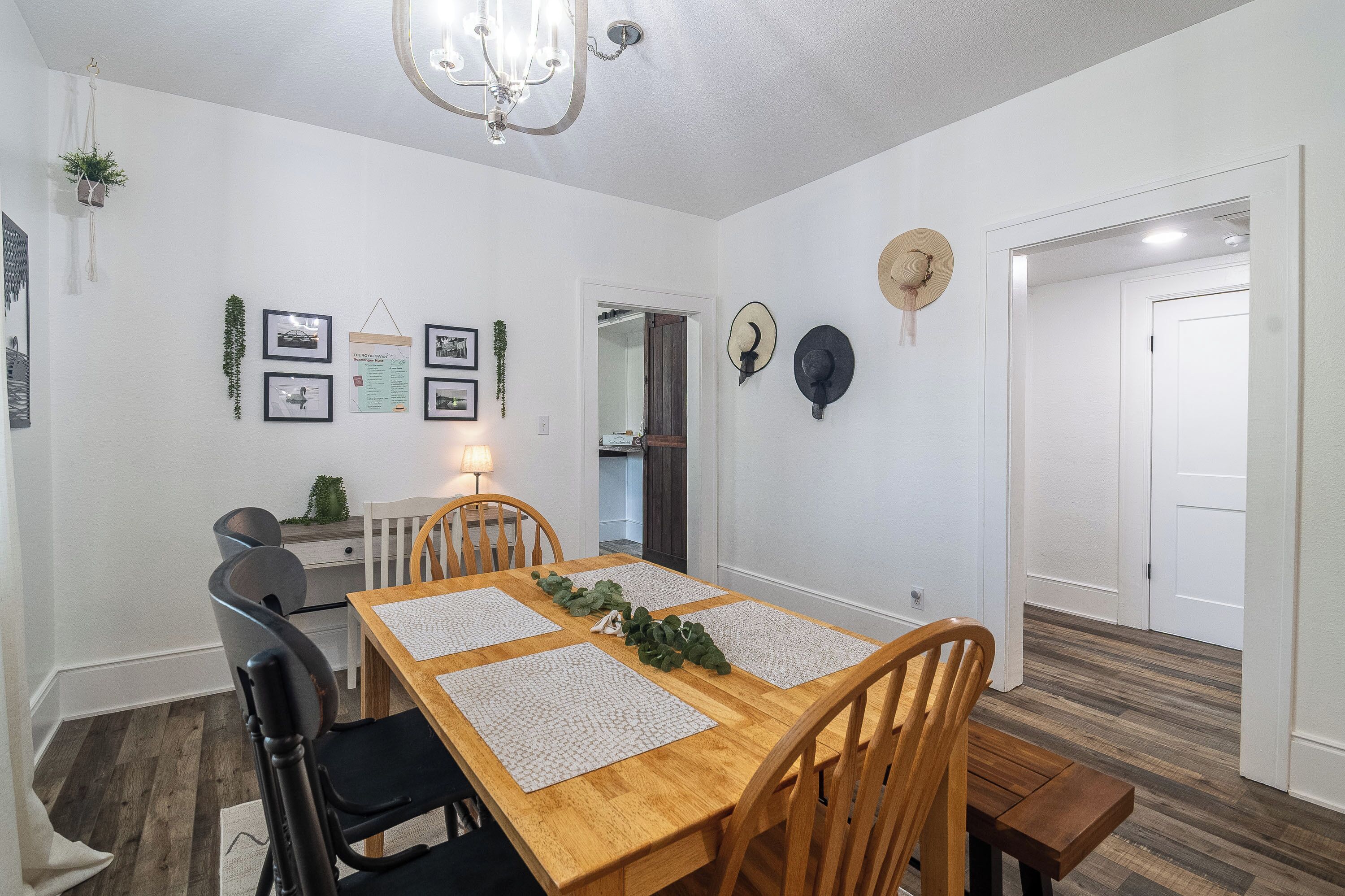 En matplats med ett träbord, fyra stolar, en kristallkrona och väggdekorationer, inklusive inramade fotografier och hattar.