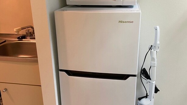 A compact kitchenette with a white refrigerator, a microwave, and a vacuum cleaner.