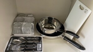A kitchen area with a stove, a pot, a cutting board, and a box of utensils.